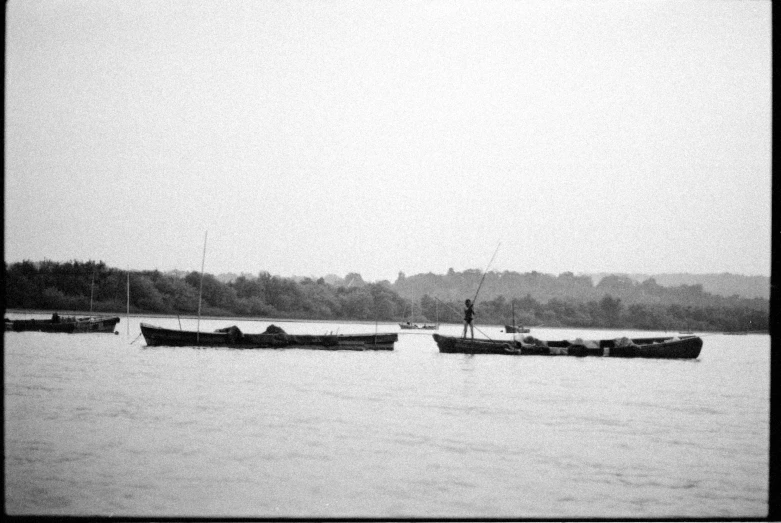 a couple of boats that are in the water, a black and white photo, by Ferenc Joachim, sōsaku hanga, nile river environment, lone person in the distance, shot on 3 5 mm film, low quality footage