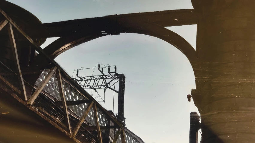 a train traveling over a bridge under a blue sky, a colorized photo, by Harvey Pratt, steel archways, louis sullivan, 1950s photograph, tangled overhead wires