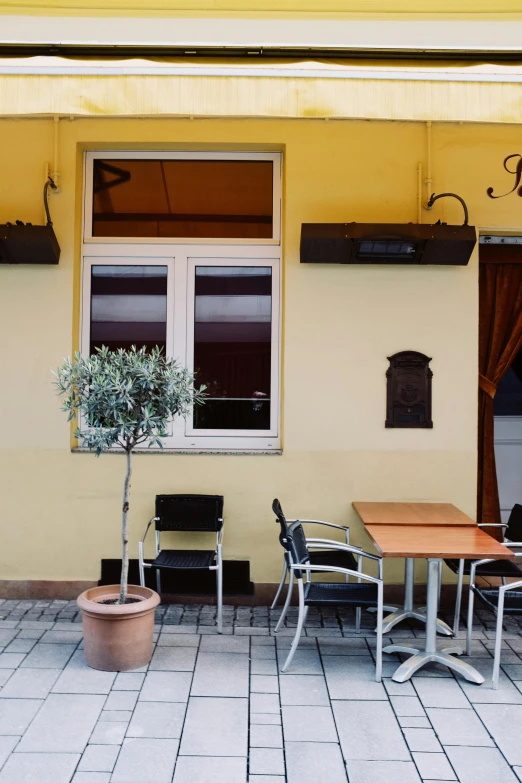 a table and chairs in front of a yellow building, a photo, renaissance, bar tosz domiczek, olive tree, brown, kino