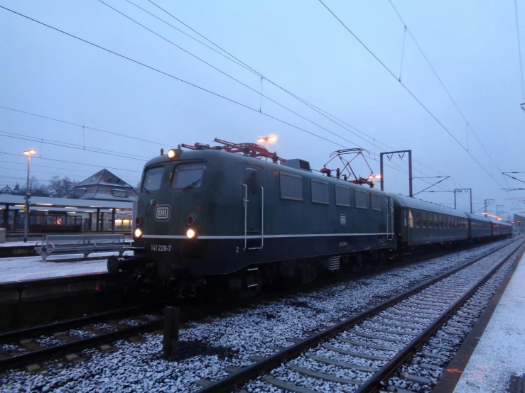 a train traveling down train tracks next to a train station, by Jens Søndergaard, hurufiyya, only snow in the background, green lightning, square, real engine