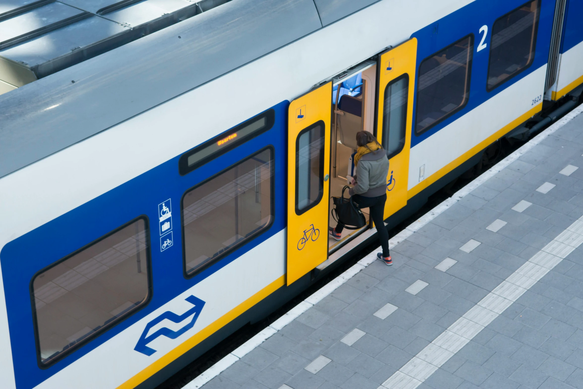 a passenger train stopped at a train station, by Jacob van Utrecht, happening, blue and yellow, person in foreground, square, no - text no - logo