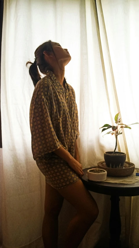 a young woman is wearing a short pyjama while standing on the window sill