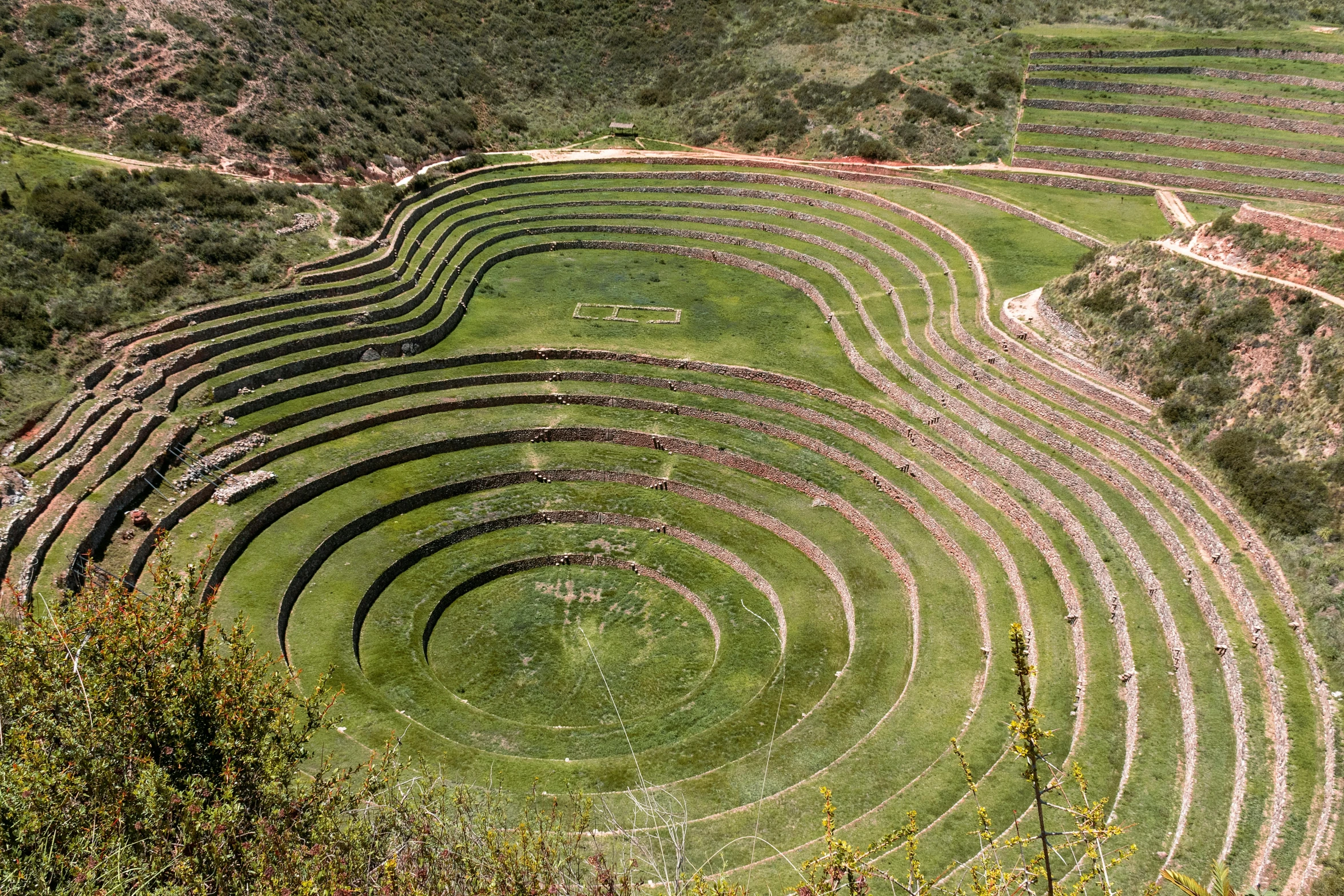 a large circular structure sitting on top of a lush green hillside, a mosaic, pexels contest winner, land art, quechua, intarsia, avatar image, mini amphitheatre