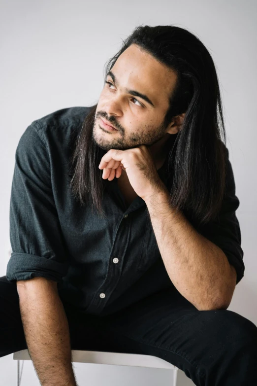 man with long hair sitting on chair looking up to side