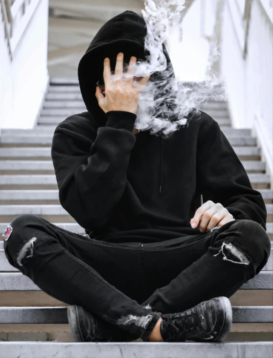 a person sitting on a stairway smokes their face with their hands