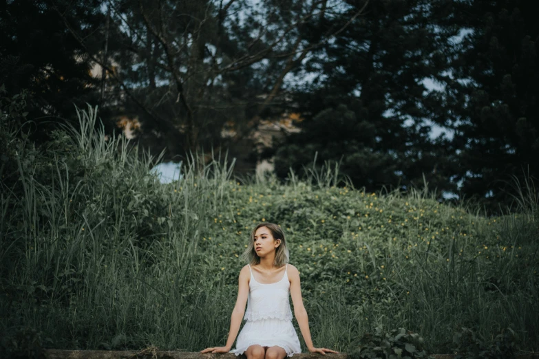 a beautiful young woman sitting on top of a log