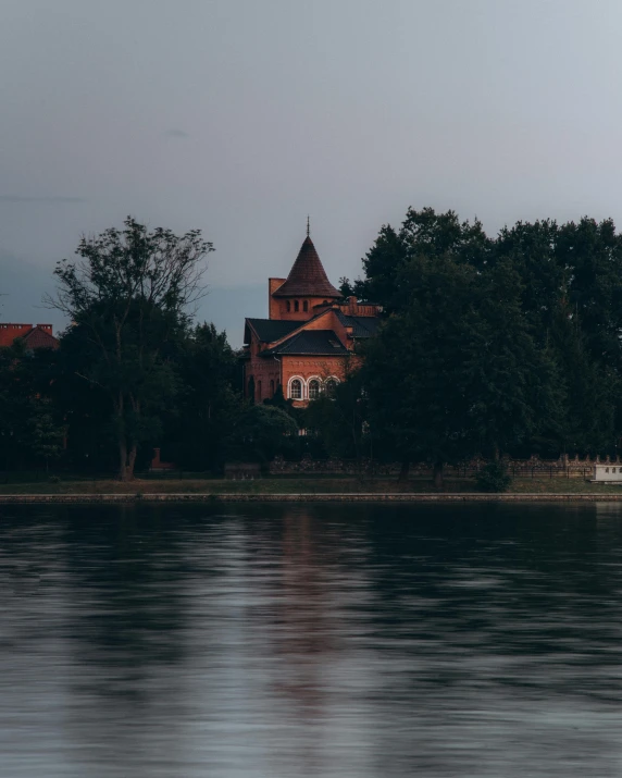 a large building sitting next to a body of water, pexels contest winner, danube school, ominous evening, against the backdrop of trees, red castle in background, instagram photo