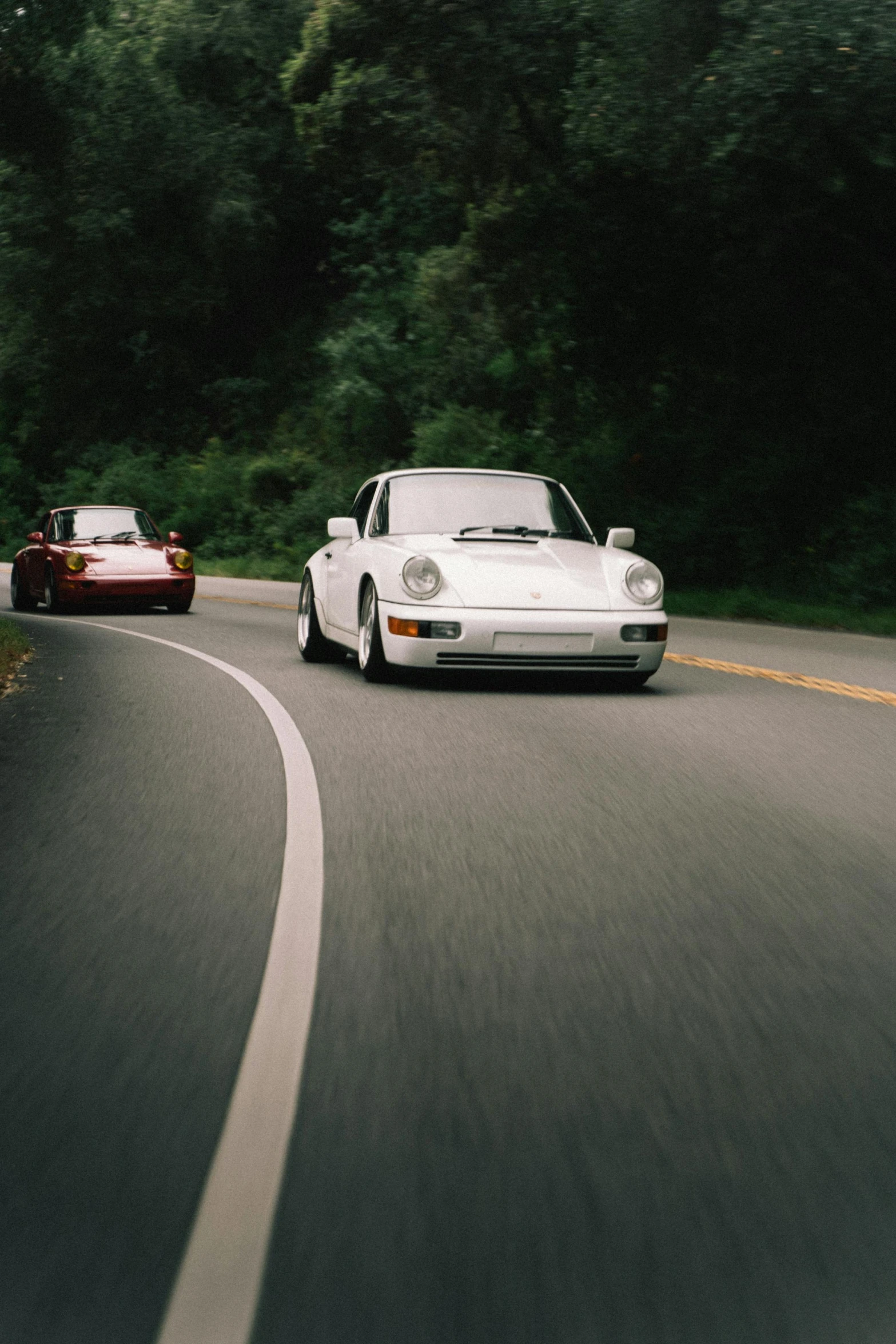 two sports cars driving down a highway with trees in the background