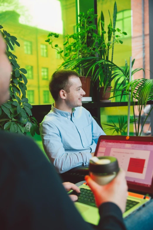 a group of people sitting around a table with laptops, by Adam Marczyński, happening, next to a plant, profile image, tarmo juhola, sitting on a mocha-colored table