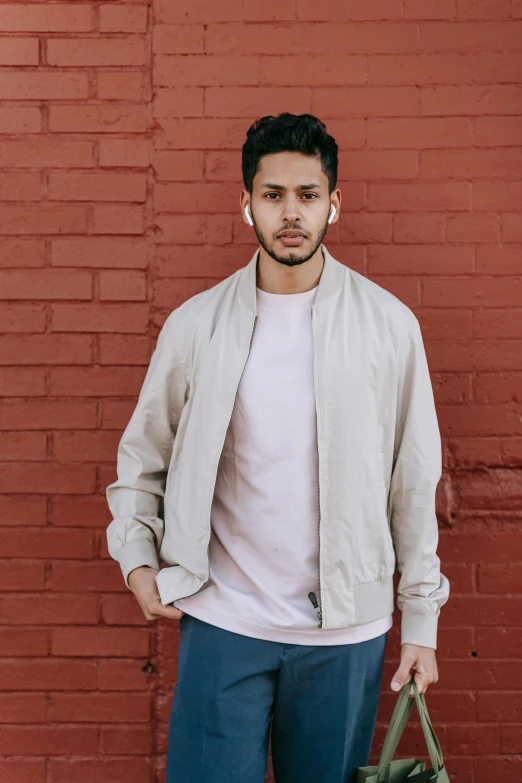 a man standing in front of a brick wall, featured on instagram, bomber jacket, light grey mist, wear's beige shirt, andrew gonzalez