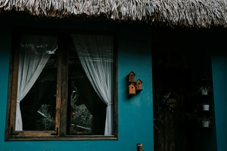 a thatched roof and wooden window on a turquoise house