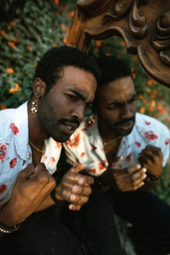 two men sitting next to each other in front of a mirror, an album cover, by Pamela Ascherson, unsplash, black arts movement, holding his hands up to his face, in the garden, donald glover, he got a big french musctache