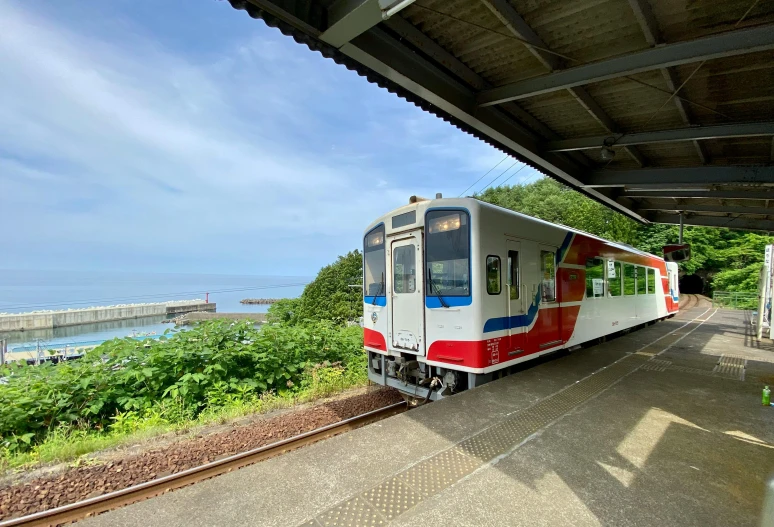 a train pulling into a train station next to a body of water, sōsaku hanga, ocean view, very colourful, s line, full device