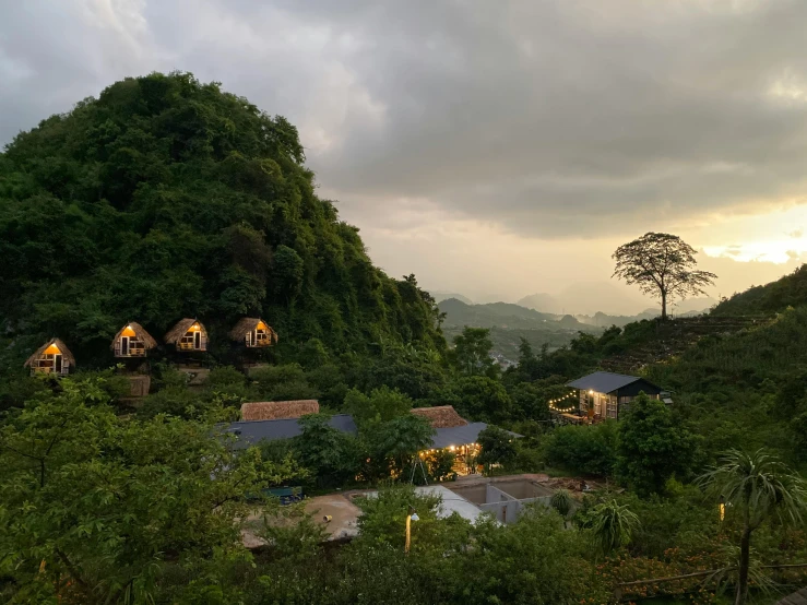 a group of huts sitting on top of a lush green hillside, evening lights, hoang lap, glamping, profile image