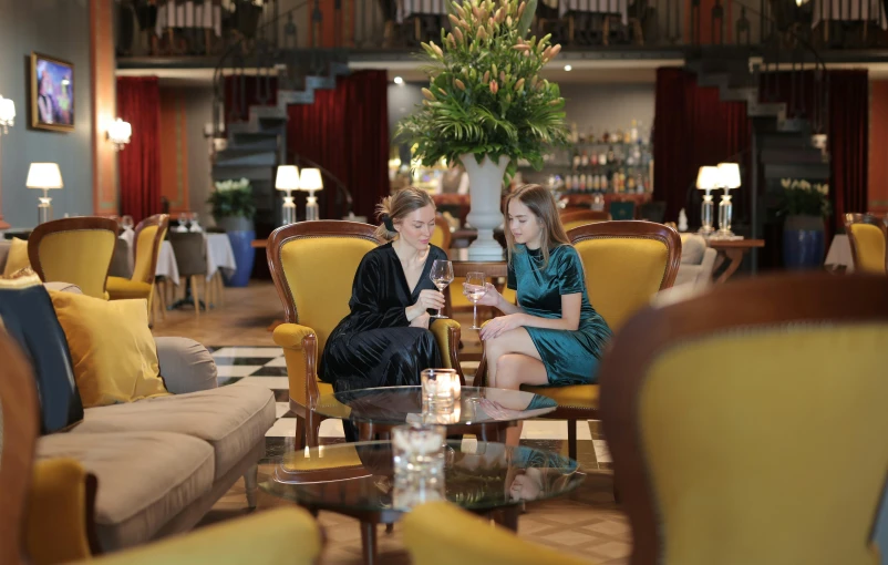 a couple of women sitting next to each other in a living room, fine dining, multiple stories, hotel, cocktail bar