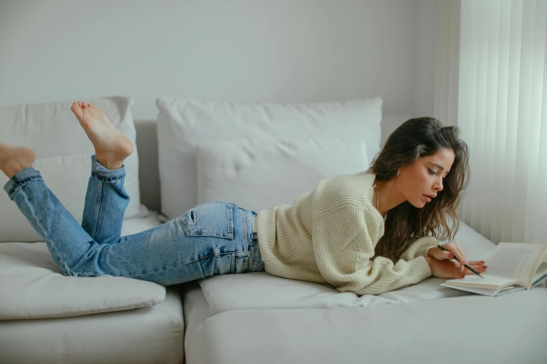 a woman laying on a couch reading a book, inspired by Elsa Bleda, trending on pexels, arabesque, wearing jeans, isabela moner, looking at his phone, writing a letter