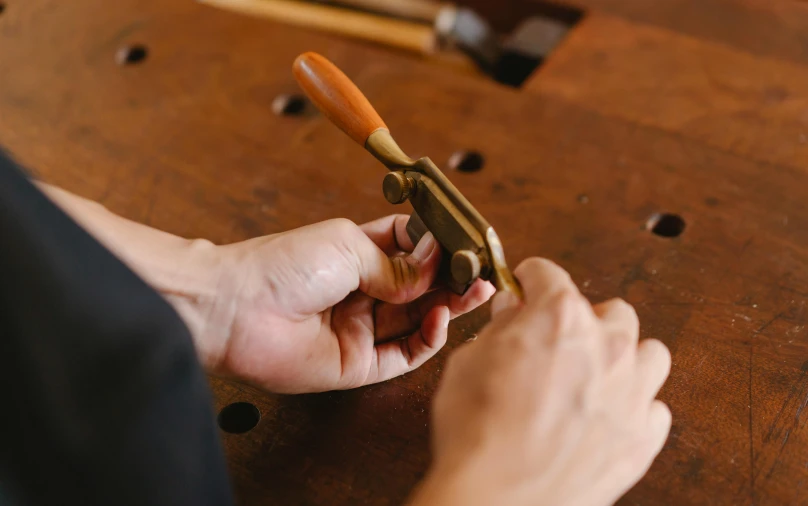 a close up of a person cutting a piece of wood, an engraving, trending on pexels, private press, brass beak, golden pommel, brown, handcrafted