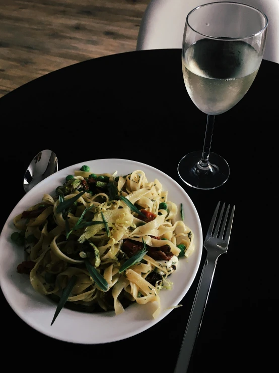 plate with pasta and wine on black table with silverware