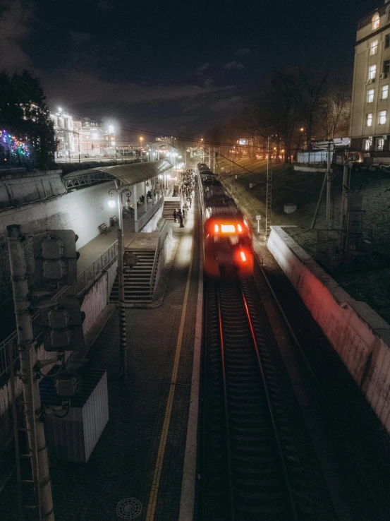 a train traveling down train tracks at night, by Alejandro Obregón, unsplash contest winner, neo kyiv, low quality photo, in the middle of the city, 2000s photo