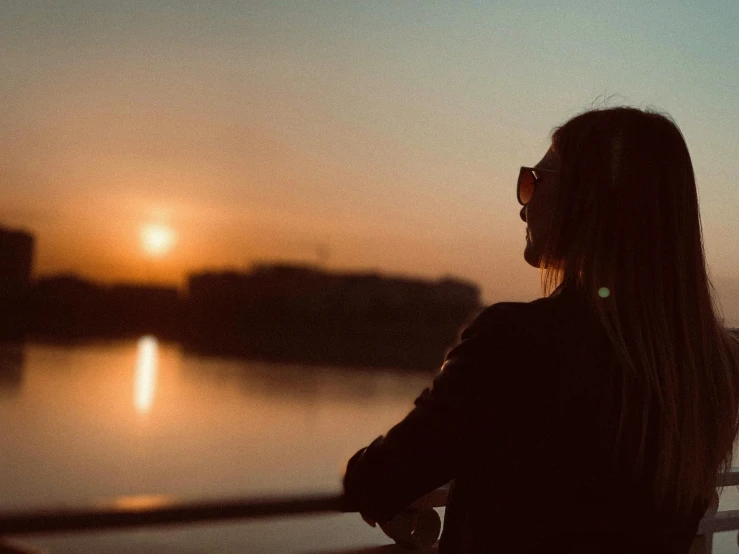 a woman looking out over a body of water at sunset, pexels contest winner, happening, woman with rose tinted glasses, silhouette :7, handsome girl, during the night