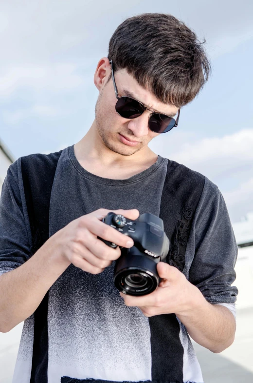 a young man wearing sunglasses holding a camera, by Adam Marczyński, professional photo-n 3, in an action pose, high quality upload, ceramic