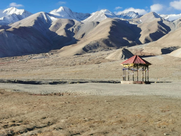 a hut in the middle of a desert with mountains in the background, by Muggur, hurufiyya, tibetan inspired architecture, gravel and scree ground, listing image, multiple stories