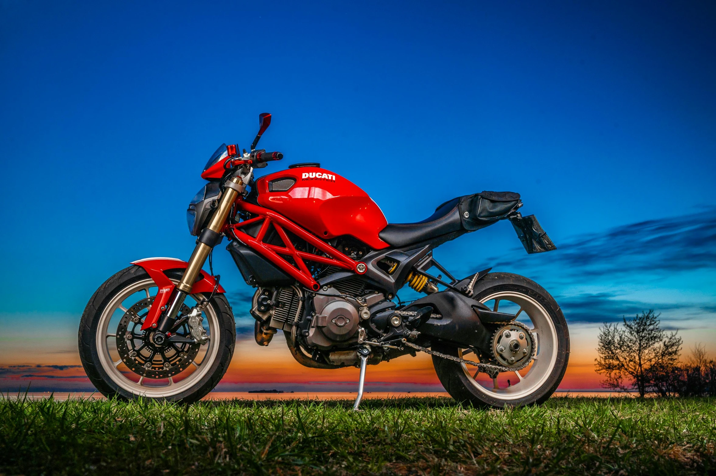 a red motorcycle parked on top of a lush green field, pexels contest winner, photorealism, sun down, huge ducati panigrale motorbike, avatar image, blue hour photography