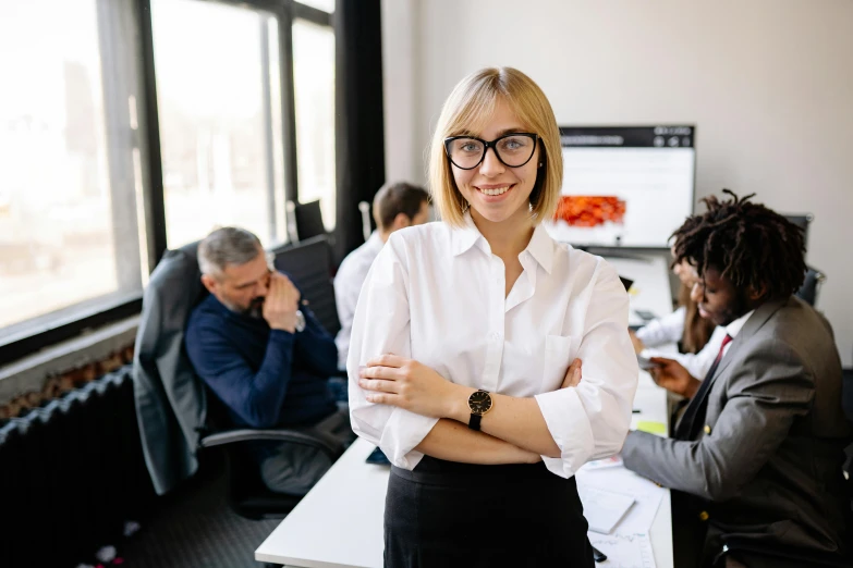 a woman standing in an office with her arms crossed, pexels contest winner, group of people, girl wearing round glasses, lachlan bailey, engineer