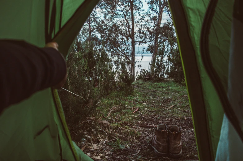 a person standing inside of a tent in the woods, views to the ocean, lachlan bailey, feet on the ground, parks and lakes