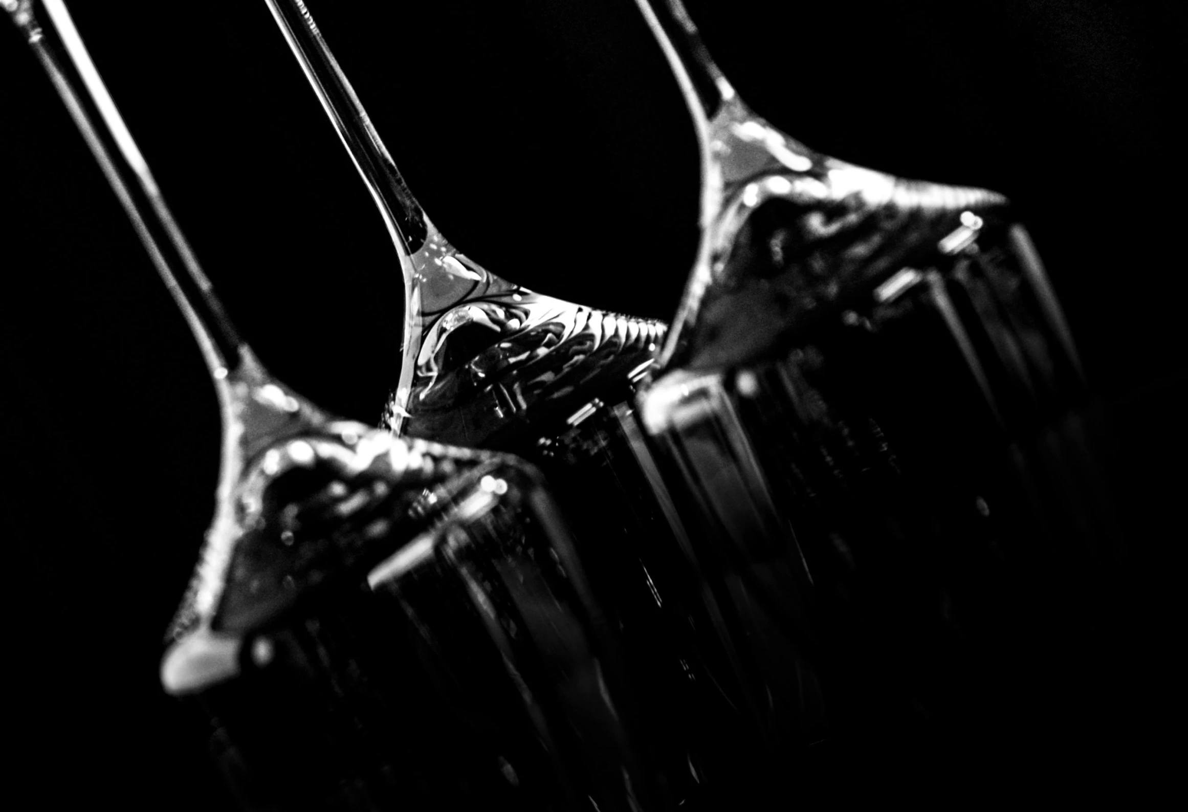 a row of wine glasses sitting on top of a table, a black and white photo, by Patrick Pietropoli, art photography, dripping black iridescent liquid, view from the bottom, trio, garnish