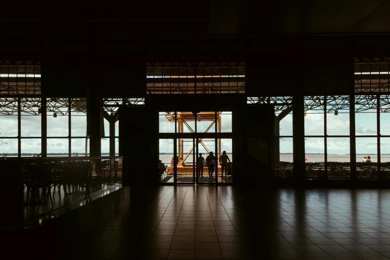 a couple of people that are standing in front of a window, pexels contest winner, hangar, people walking into the horizon, brown, indoor setting