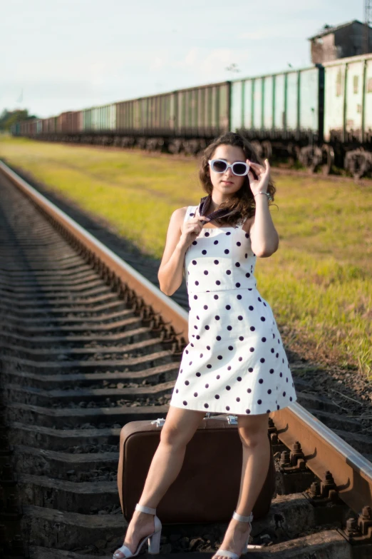 woman sitting on rail road tracks in polka dot dress and sunglasses