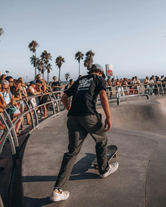 a man riding a skateboard up the side of a ramp, pexels contest winner, happening, in front of a large crowd, tan skin a tee shirt and shorts, standing near the beach, wearing a black t-shirt