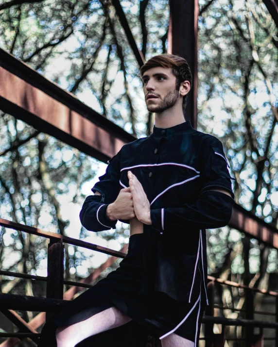a man that is standing on some stairs, an album cover, by Alejandro Obregón, unsplash, renaissance, attractive androgynous humanoid, karate outfit, black clothing, against the backdrop of trees