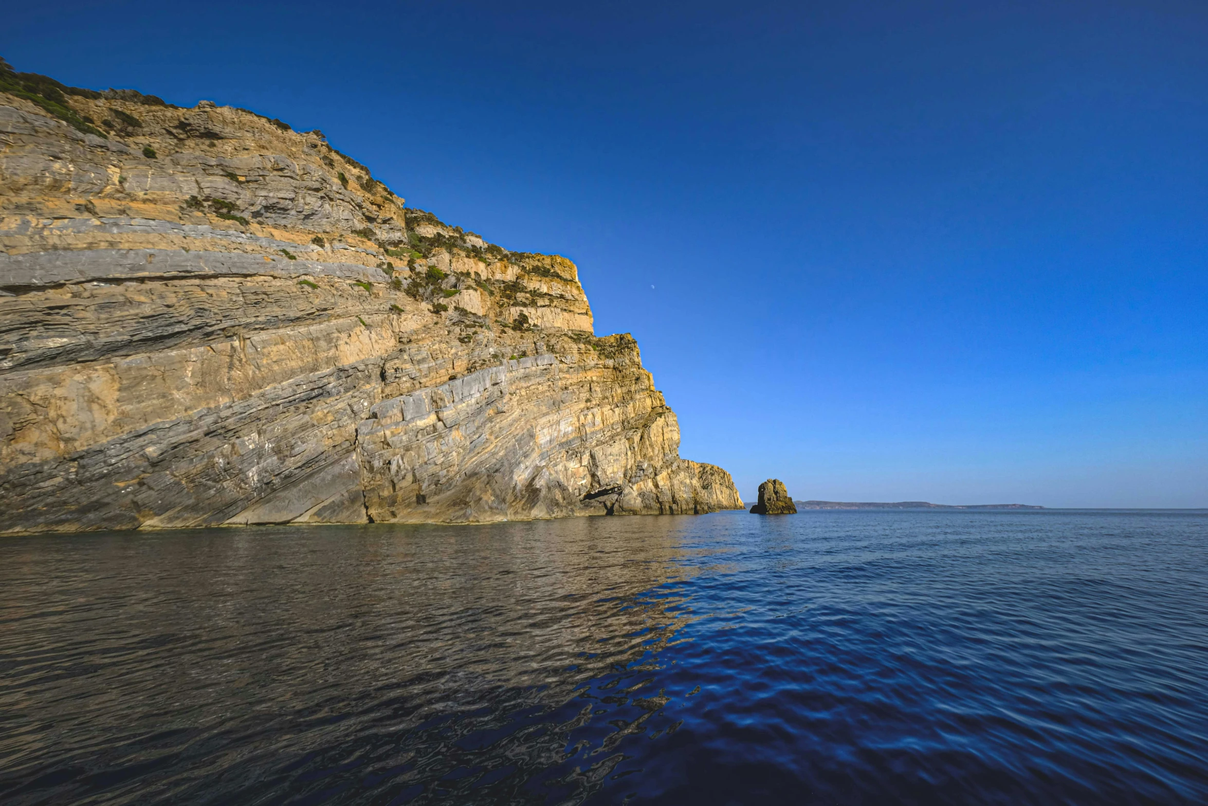 a very large rock cliff on top of a body of water