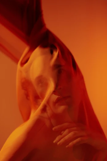 a naked woman standing in front of a mirror, an album cover, inspired by Anna Füssli, unsplash, swirling red-colored silk fabric, ryan mcginley, orange light, hood and shadows covering face