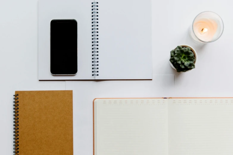 a cell phone sitting on top of a notebook next to a candle, trending on unsplash, minimalism, on white paper, background image, mixed materials, minimalist desk