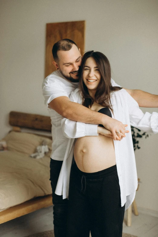 a pregnant woman standing next to a man in a white shirt, pexels contest winner, couple on bed, supportive, gif, belly