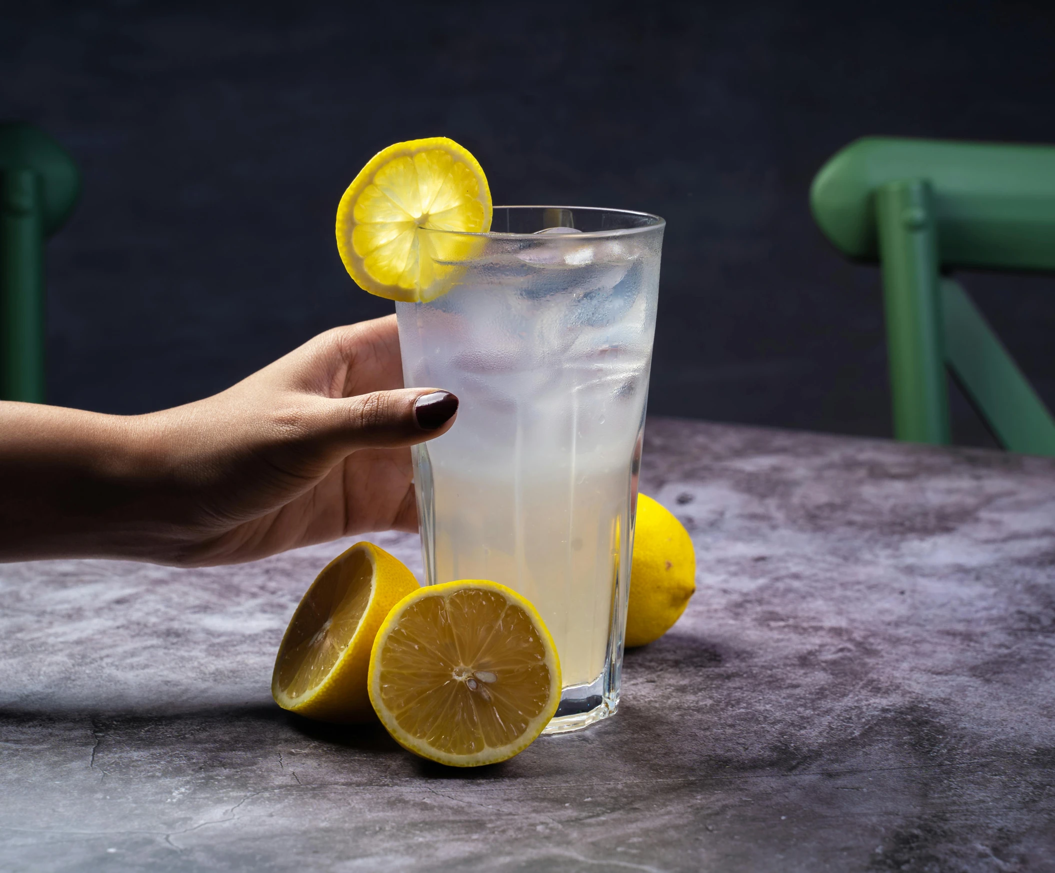 a person holding a glass of lemonade on a table, trending on pexels, photorealism, against dark background, angled, background image, opening shot