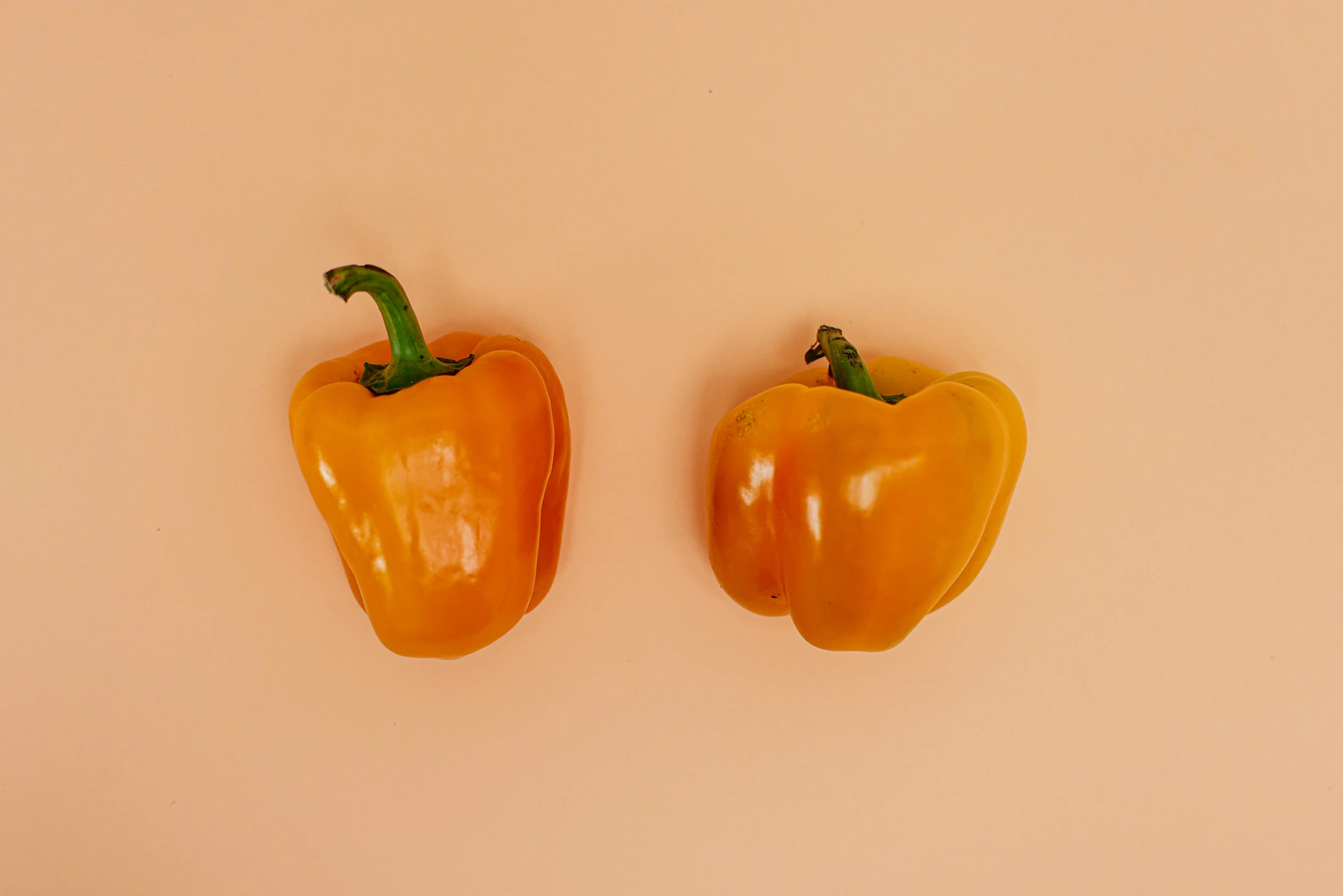 two orange peppers sitting next to each other on a pink surface, by Kristin Nelson, trending on pexels, light tan, chilean, background image, 6 pack