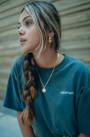 a woman sitting in front of a wooden wall, by Anthony Devas, unsplash contest winner, graffiti, wearing a marijuana t - shirt, multiple golden necklaces, profile image, loose braided hair