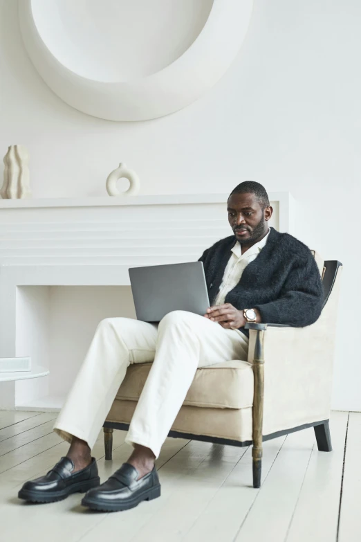 a man sitting in a chair using a laptop, kevin garnett, in a white room, cozy environment, ignant