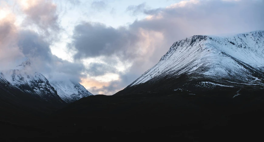 the clouds are gathering around mountains with some snow