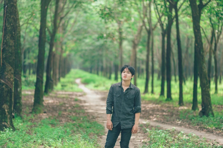 a boy standing on a dirt road near a forest