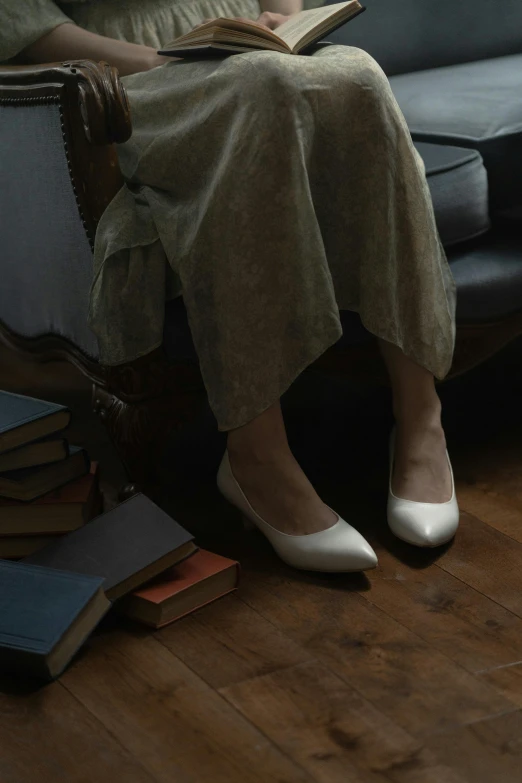 a woman sitting on a couch reading a book, inspired by Balthus, renaissance, white shoes, standing in a dimly lit room, promo image, white pearlescent