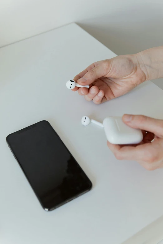 a white table topped with an apple airpods next to a cell phone, by Adam Marczyński, happening, hand on table, artificial, operation, product view