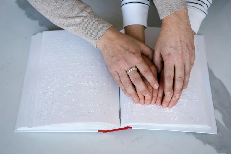 a person with their hands on an open book, two people, touching, on a white table, marfan syndrome