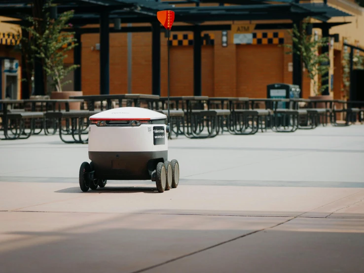 a white and black robot sitting on top of a sidewalk, cart, square, circular, vehicle