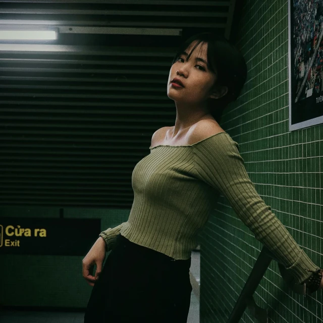 a woman leaning against a wall in a subway station, an album cover, inspired by Elsa Bleda, pexels contest winner, realism, asian girl, wearing a cropped top, wearing a green sweater, cynthwave