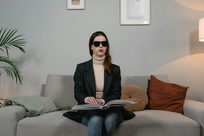 a woman sitting on a couch reading a book, an album cover, by Emma Andijewska, trending on pexels, visual art, implanted sunglasses, lie detector test, girl in suit, non binary model